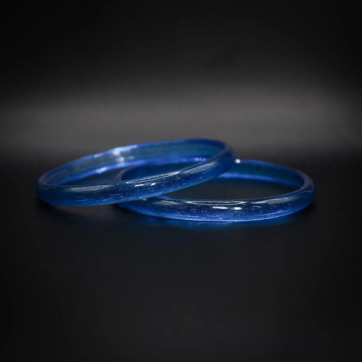 Par ljusblå glasarmband i transparent himmelsblått glas, vikingatida reproduktion mot mörk bakgrund
