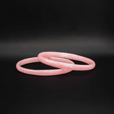 Två rosa glasarmband med spräcklig yta liggande omlott mot svart bakgrund