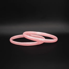 Två rosa glasarmband med spräcklig yta liggande omlott mot svart bakgrund