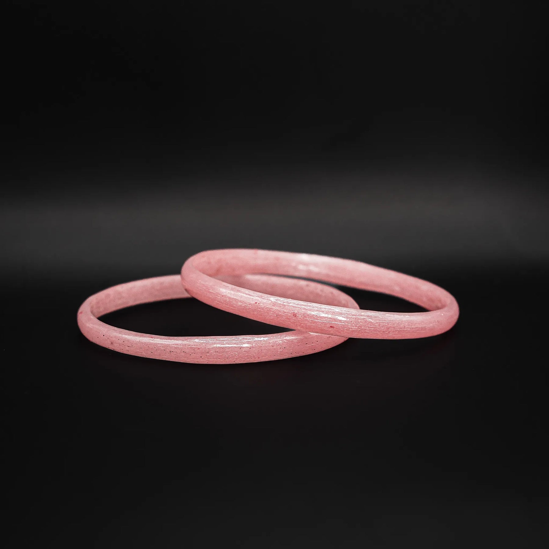 Närbild av två rosa glasarmband med matt spräcklig textur mot mörk bakgrund