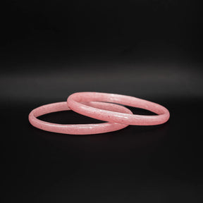 Närbild av två rosa glasarmband med matt spräcklig textur mot mörk bakgrund