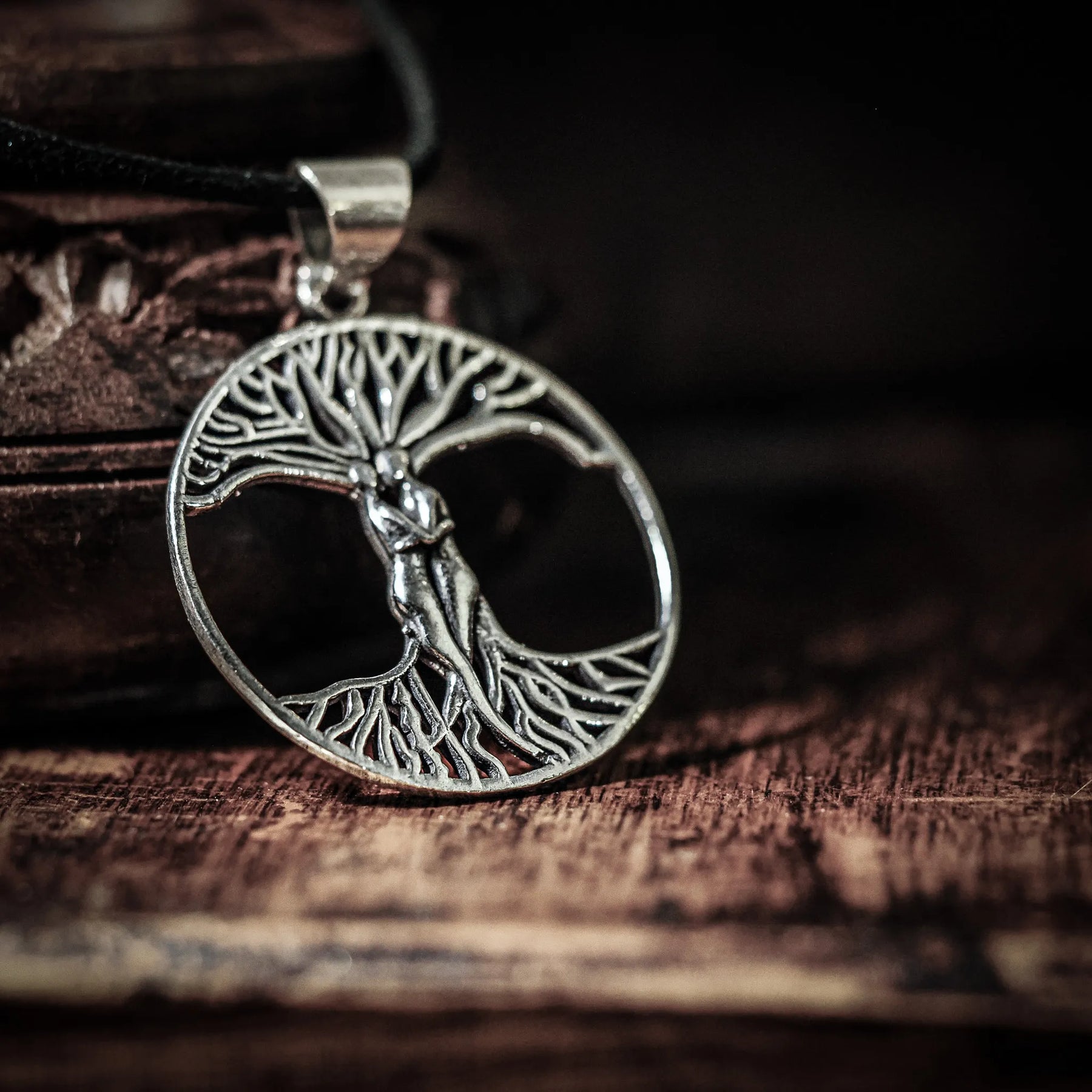 Stor träd-amulett på brunt läderband mot träbakgrund, visar Yggdrasil-motivet med naturlig, vikingartsmyckestil.