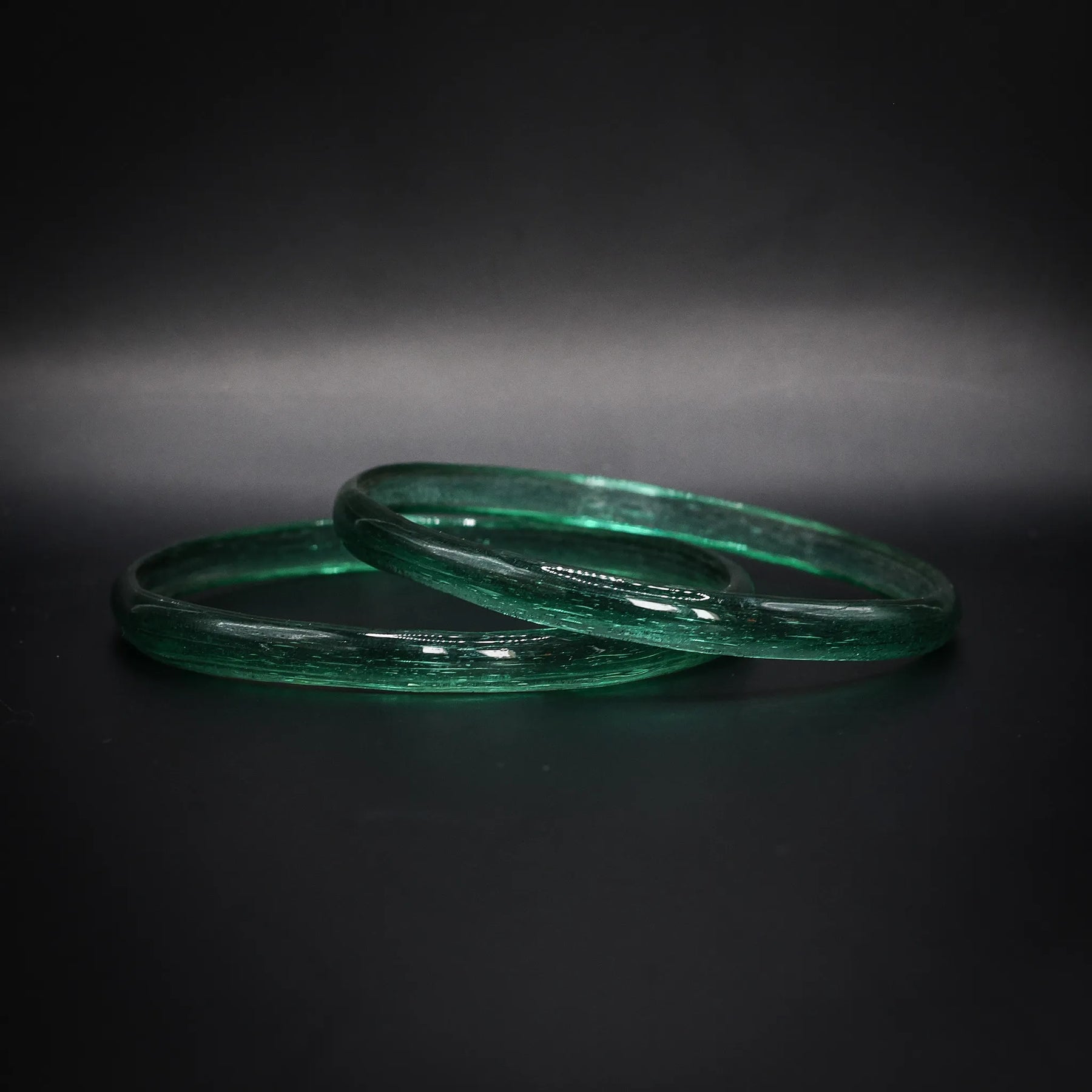 Par gröna glasarmband med genomskinlig struktur, vikingatida reproduktion mot mörk bakgrund