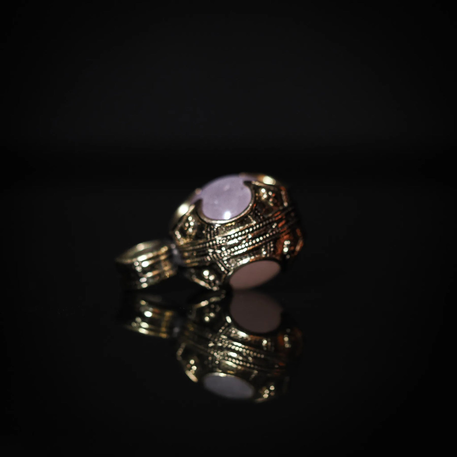 Gotlandshänge-hänge i mässing med rosa kvarts, fotograferat från sidan för att visa djup och textur. Detaljerade linjemönster och stämplad dekoration på hela metallramen.