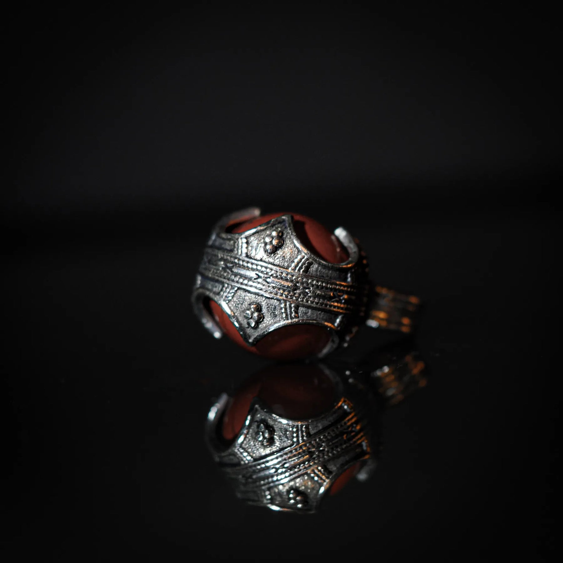 Mässingshänge med röd jaspis i tre-fjärdedels vy. Ornerad brassmålad metall med detaljerad ytstruktur. Glansig röd jaspis-sten med klassiska vikingamönster i kapsylen.
