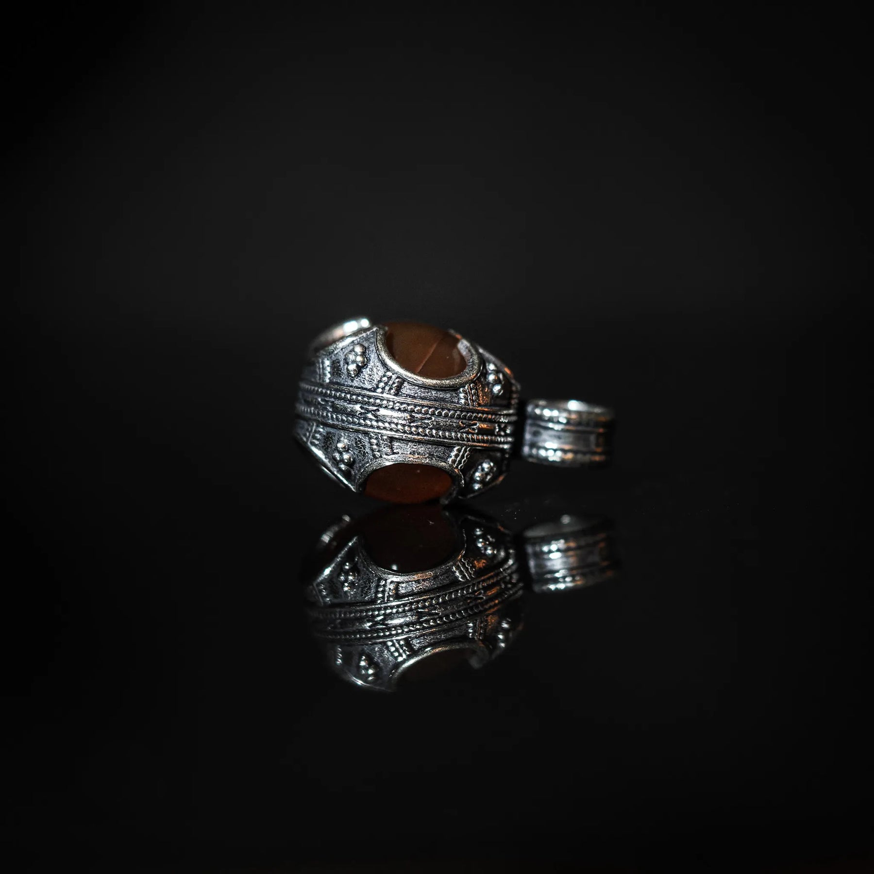 Ornerad silverpläterad vikingahänge med rödagat. Detaljerad linjemönstrad metall med glansig sten i klassisk design. Matching sling-ring synlig bredvid.