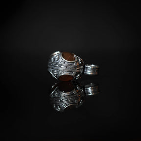 Ornerad silverpläterad vikingahänge med rödagat. Detaljerad linjemönstrad metall med glansig sten i klassisk design. Matching sling-ring synlig bredvid.