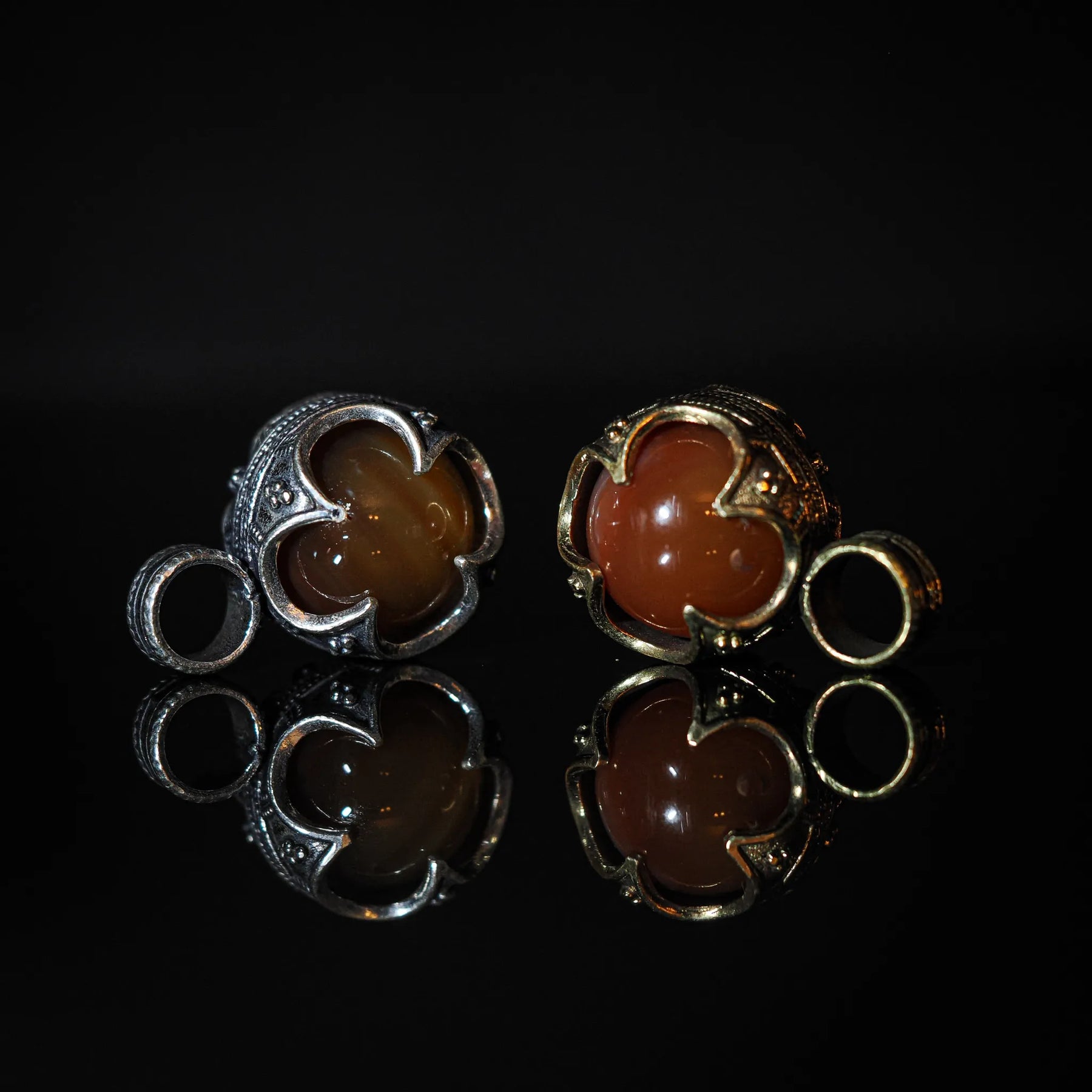 Två silverpläterade och två mässingspläterade Gotlandshängen med rödagat-stenar. Symmetrisk jämförande display av varianterna i klassisk vikingastil. Små sling-ringar bredvid varje par.