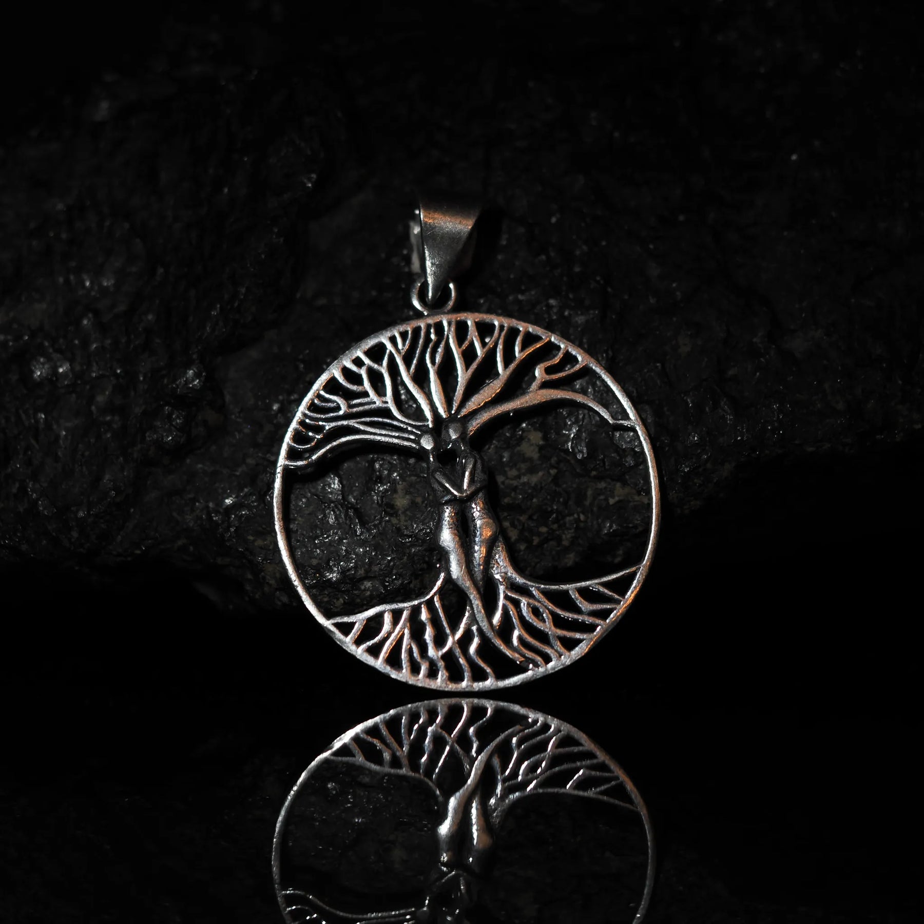 Stor träd-amulett på silverkedja fotograferad mot svart bakgrund med reflektion, visar Yggdrasil med fina detaljer i grenar och rötter.