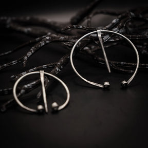 Två stålringnålar med polerad finish på mörk textil