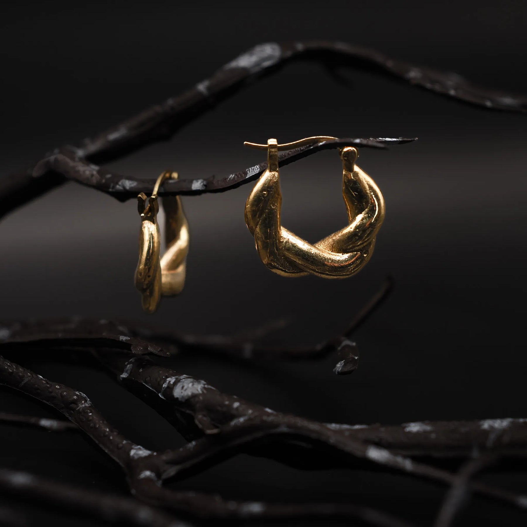 Närbild på flätad örhänge i guldöverlagring, cirka 2 cm stor, visar väven och metallglansen tydligt