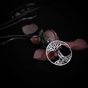 Träd-amulett på silverkedja liggande på torkade rosor och blad, skapar mystisk vikingartmosfer.