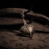 Bronshänge i form av vikingaskepp med drakehuvud vid förskepp. Hängande från svart lädersnöre. Detaljerad metallarbete med varm glans.