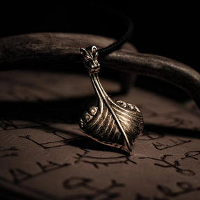 Bronshänge i form av vikingaskepp med drakehuvud vid förskepp. Hängande från svart lädersnöre. Detaljerad metallarbete med varm glans.