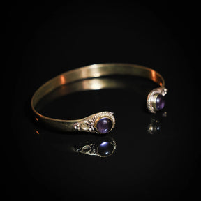 Brass dubbelarmband med lapis lazuli-stenar, visa från sidan med dramatisk belysning som framhäver stenens lysglans och mässingens finish.