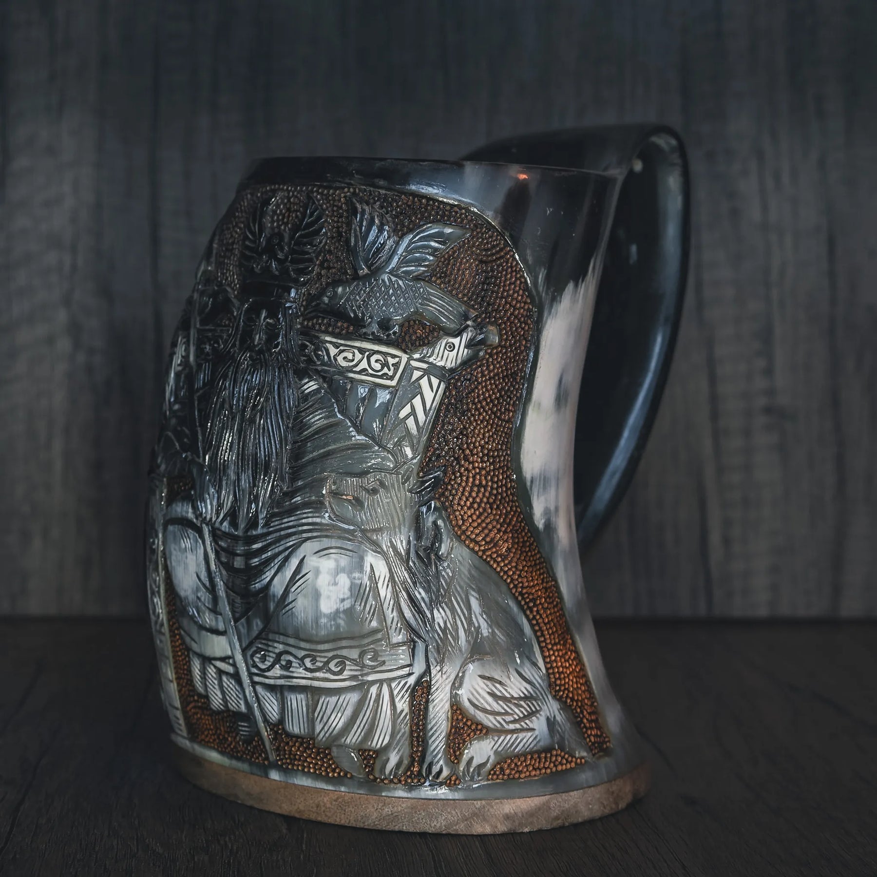 Sidovy av handsnidad hornmugg med Allfader Odens graverade porträtt. Visar tredimensionell gravering med djup och relief. Mässingsband synligt vid basen. Naturlig hornfärg med ljusare kornmönster och polerad yta.