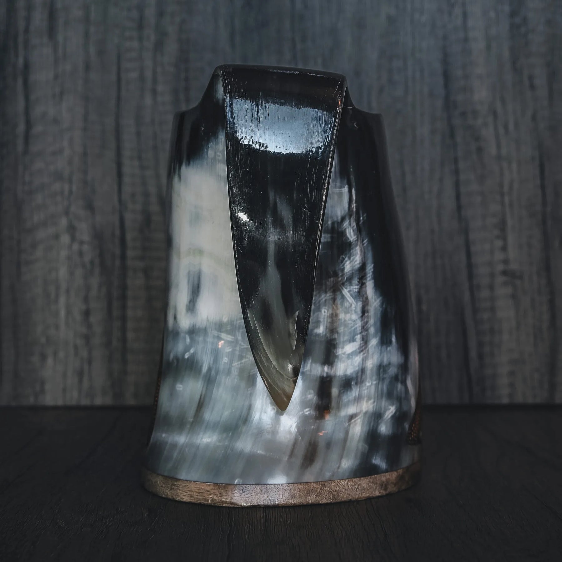 Frontvy av handsnidad hornmugg med konisk form och naturlig hornfärg. Visar den karakteristiska spetsiga basen och hornets naturliga kornstruktur. Trädäband vid kanten. Tjockt, organiskt horn utan gravering.