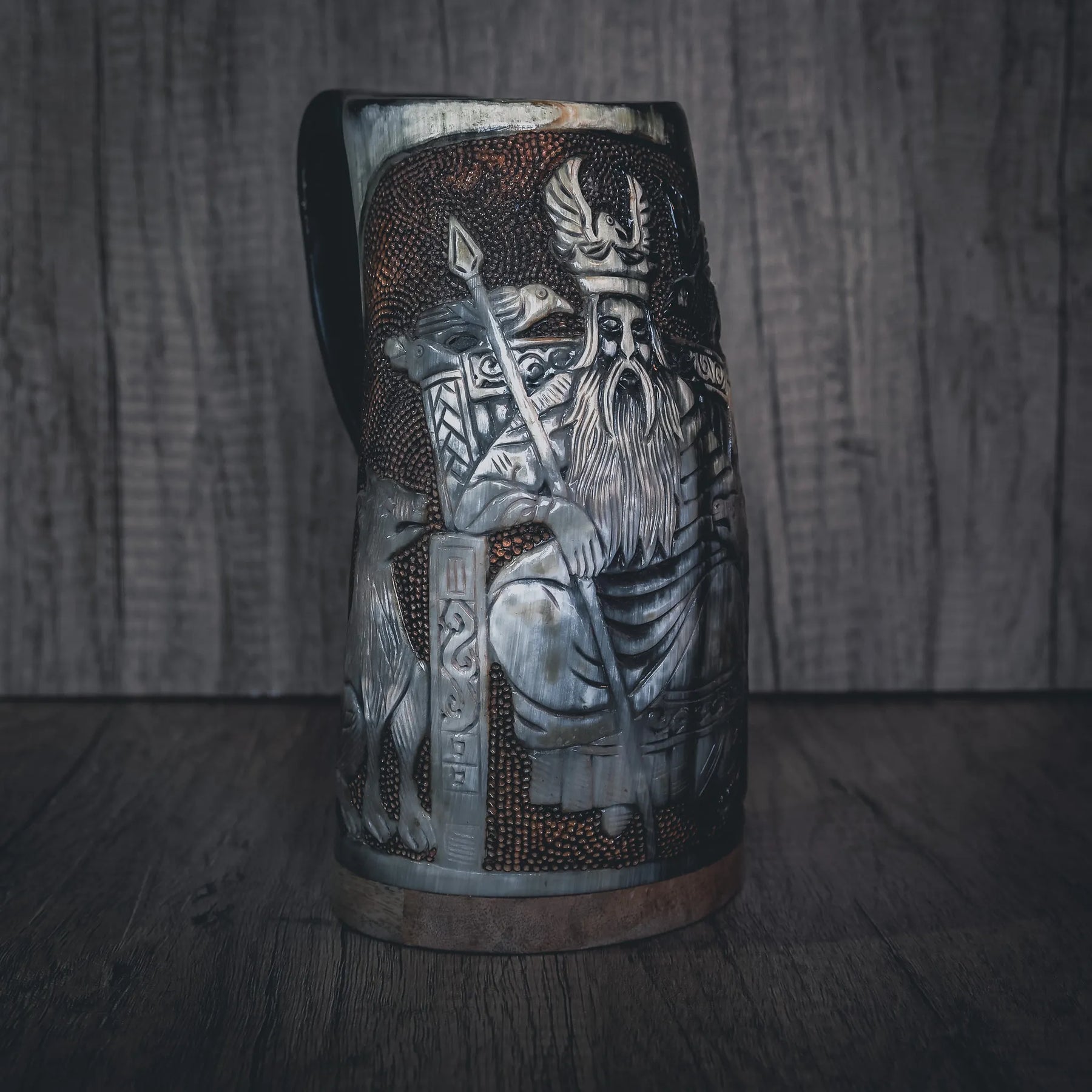 Handsnidad hornmugg med stor Odin-figur i högt relief. Stående krigarfigur med detaljerade kläder, långt skägg och hållande vad som verkar vara en stav eller spjut. Komplex komposition med Odin som centralfigur omgiven av ytterligare snidelement och mönster. Naturligt horn med utmärkt relief definition. Kopparband vid basen.