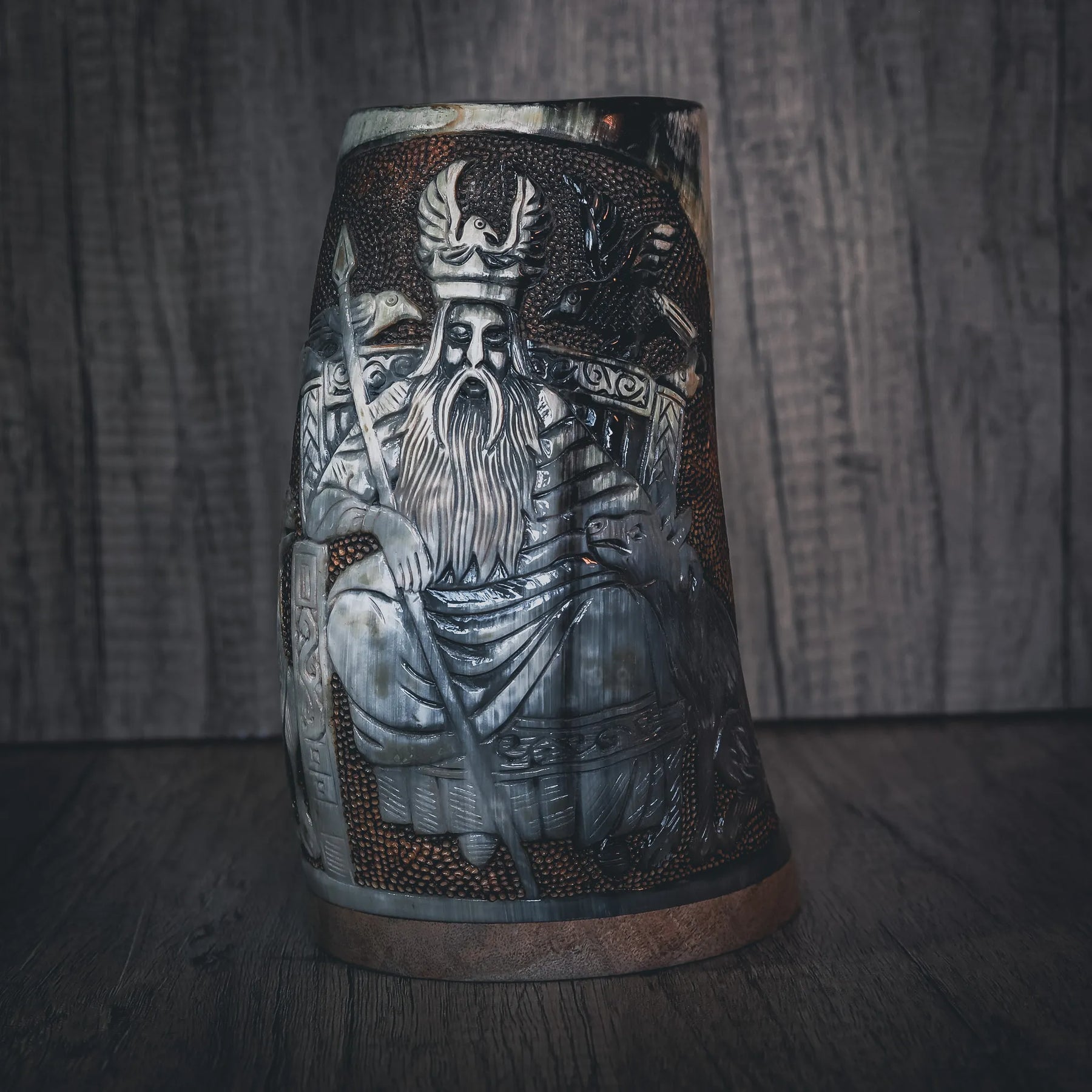 Handsnidad hornmugg med frontvy av Odin-ansikt i högt relief. Skäggig krigarfigur bär antilophornkrona. Intrikat geometriskt mönsterarbete i nordisk stil fyller ytan omkring huvudfiguren. Naturligt horn med stark färgkontrast mellan graverad och polerad yta. Kopparband vid basen. Museistandard snidning med exceptionell detalj.
