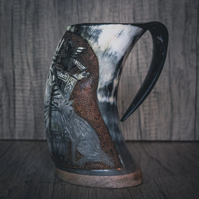 Handsnidad hornmugg visad från sidan med detaljerad reliefsnidning av Odin-ansikt. Bred skägg och intrikat mönsterarbete på ytan. Naturligt horn med varierande färg. Mörkad handtag och kopparband vid basen. Studiolysning belyser sniddetaljerna tydligt.