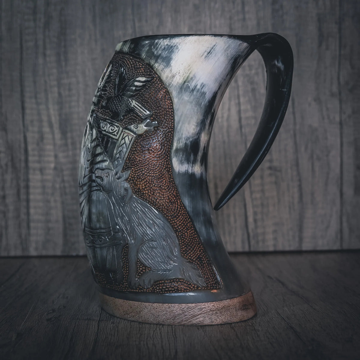 Sidovy av handsnidad hornmugg med Allfader Odens relief-gravering. Visar profilen av den skäggiga nordiska guerrafiguren. Mässingsband vid basen och handformad handtag. Naturligt hornmaterial med ljusare translucentområden.