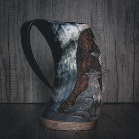 Tre-fjärdedelvy av handsnidad hornmugg med Allfader Odens graverade porträtt. Visar skäggig krigarfigur med hornad hjälm och ornamenterad bröstharnask. Handformad handtag och mässingsband vid basen. Tjockt, naturligt hornmaterial med kornstruktur.
