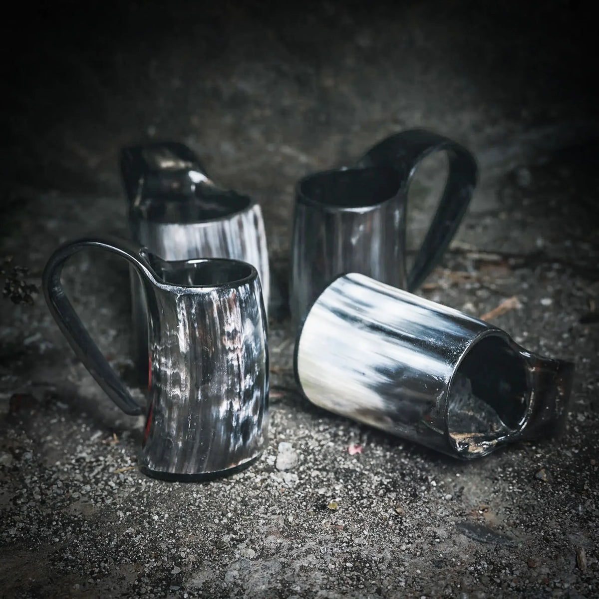 Tre handgjorda espresso- och glöggnuggar i horn arrangerade på grå betong, visar naturlig textur och glans.