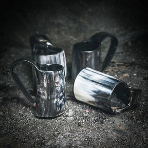 Tre handgjorda espresso- och glöggnuggar i horn arrangerade på grå betong, visar naturlig textur och glans.