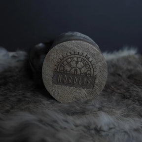 Närbild av hornmuggans botten med snidad mästarmark innehållande Nordiska runor och geometrisk ornament. Grova hornkorn och patina synlig.