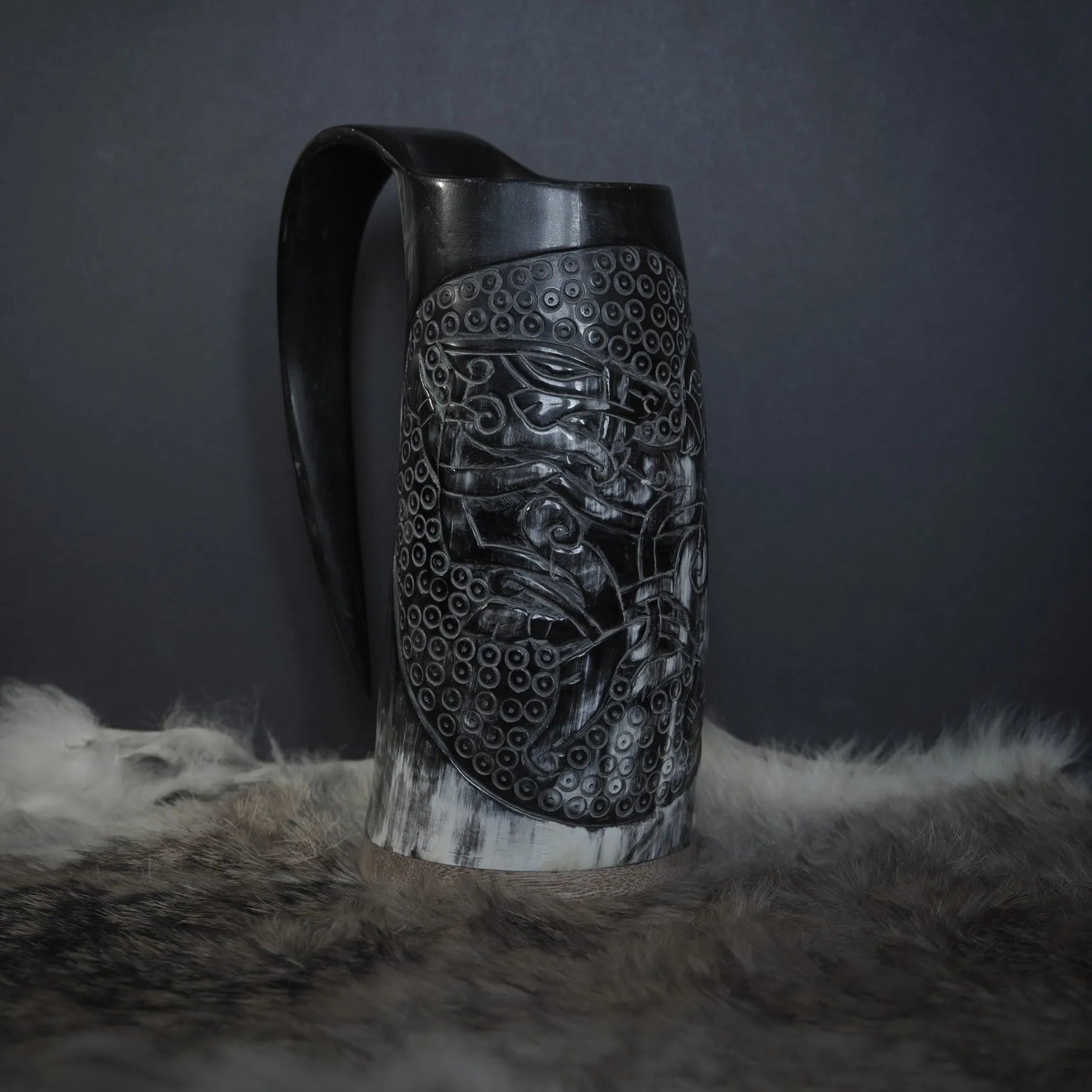 Hornmugg från framsidan med handsnidad Tyr och Fenris mytologi omgiven av precis prickmönster. Naturlig horn färg med synliga växtringar. Svart handtag.