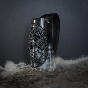 Hornmugg i ren sidoprofil. Svart handtag med ergonomisk kurva. Snidad Tyr och Fenris motiv med ornamental prickmönster synlig.