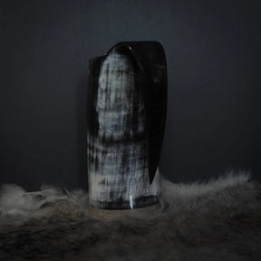 Hornmugg från tre-fjärdedels baksidvinkel. Svart handtag. Delvis syn av Tyr och Fenris sniderier med prickmönster.