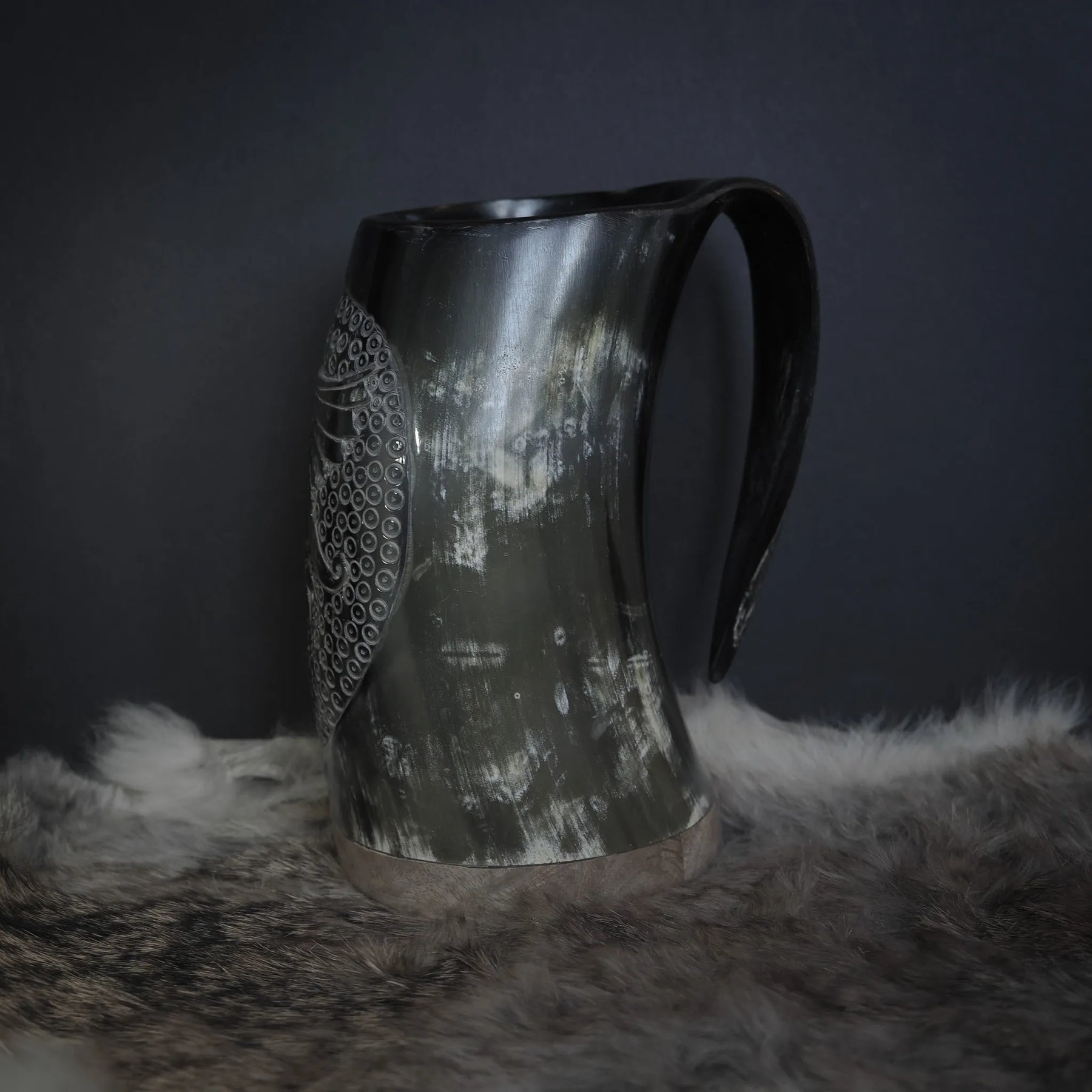 Hornmugg med handkarvad dekor visad i trevärtsvy. Naturlig horn med polerad finish, tydlig handtag och rakkarvad Hugin/Munin-motiv omgiven av prickbroderi.