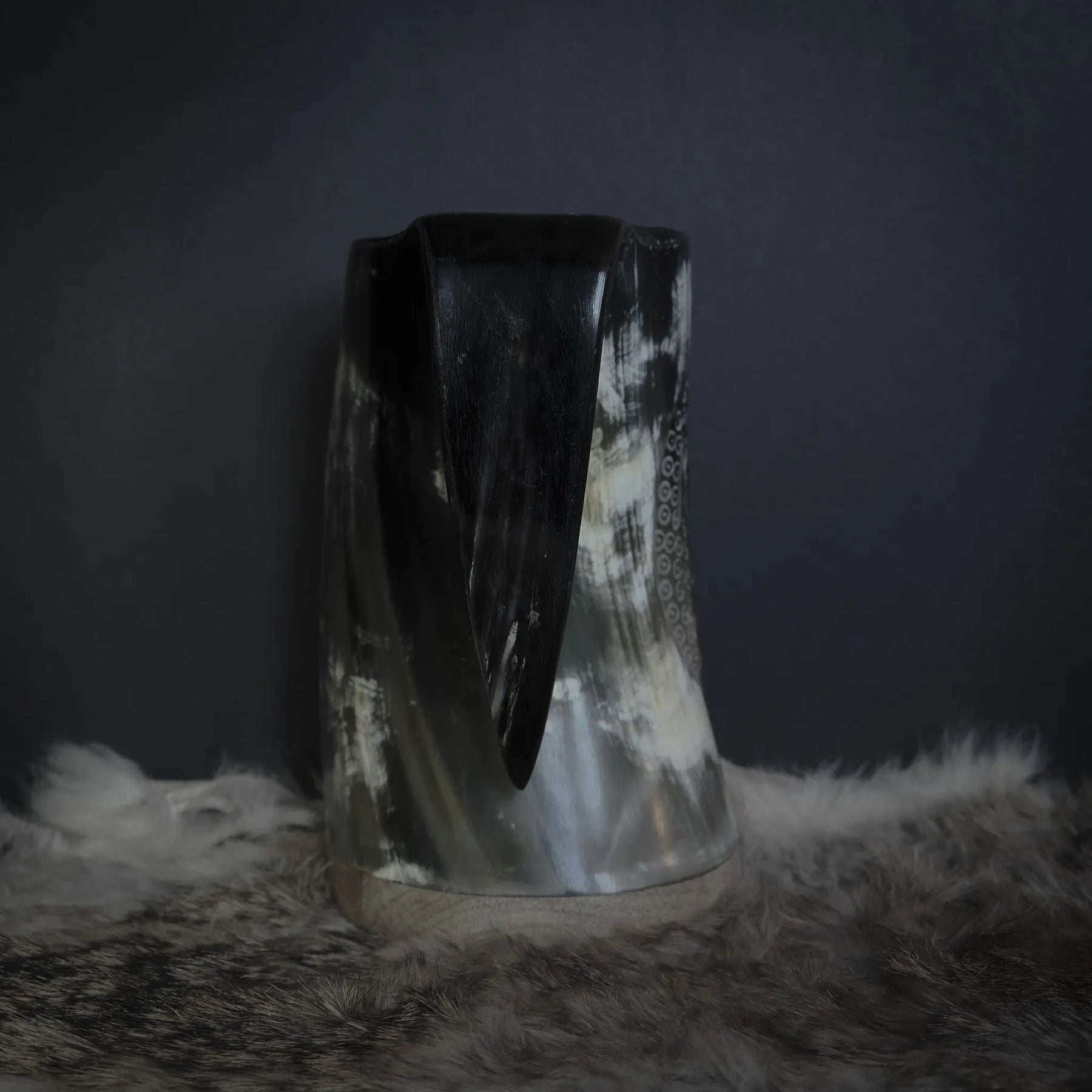 Handkarvad hornmugg visad framifrån. Dekorativ körpfågelmotif med fjäderdetaljer i mitten, omgiven av småprickat mönster. Horn i naturlig färg med ljusa och mörka strimmor.