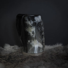 Handsnidad hornmugg med både Hugin och Munin-korpar karvade i ett band. Detaljer visar båda fåglarnas fjädrar och ett omfattande prickmönster. Naturlig horn med handtag väl synligt från denna vinkel.