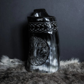 Hornmugg från tre-fjärdelsvinkel med både Livets träd och keltisk knutdesign synlig. Svart polerat horn med skarp gravering. Handtaget sträcker sig upp från sidan.