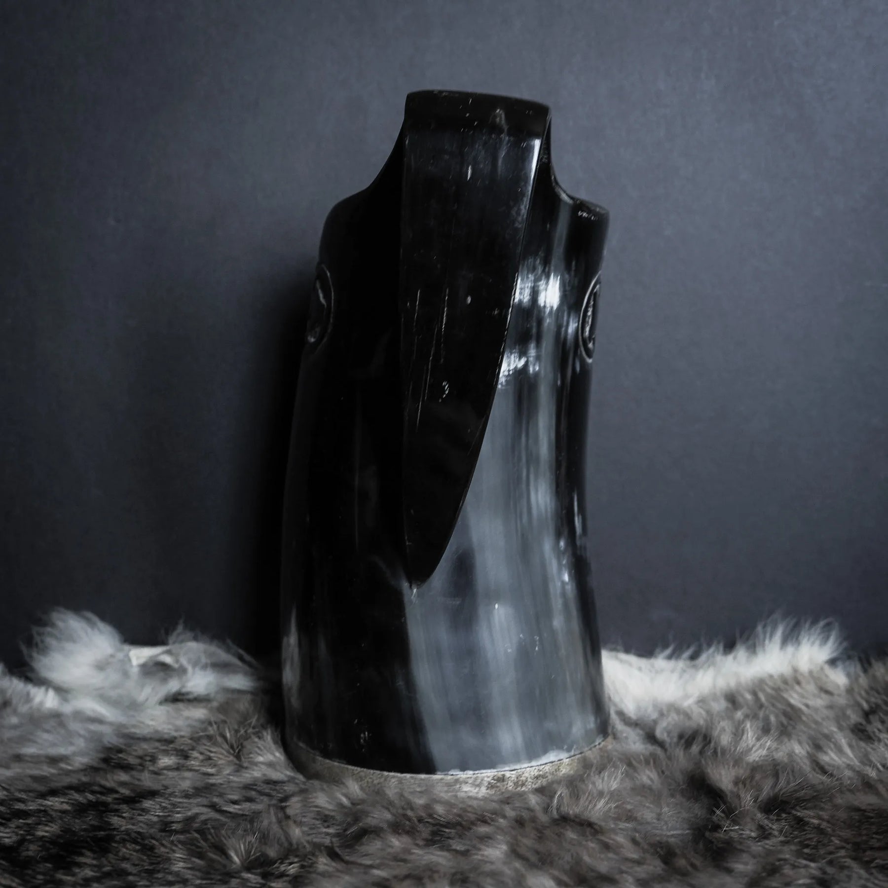 Hornmugg från sidan med fokus på den böjda handtaget. Svart polerad horn utan synlig gravering från denna vinkel. Muggens öppning synlig överst.