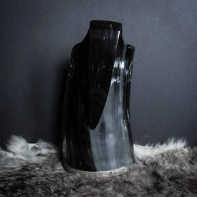 Hornmugg från sidan med fokus på den böjda handtaget. Svart polerad horn utan synlig gravering från denna vinkel. Muggens öppning synlig överst.