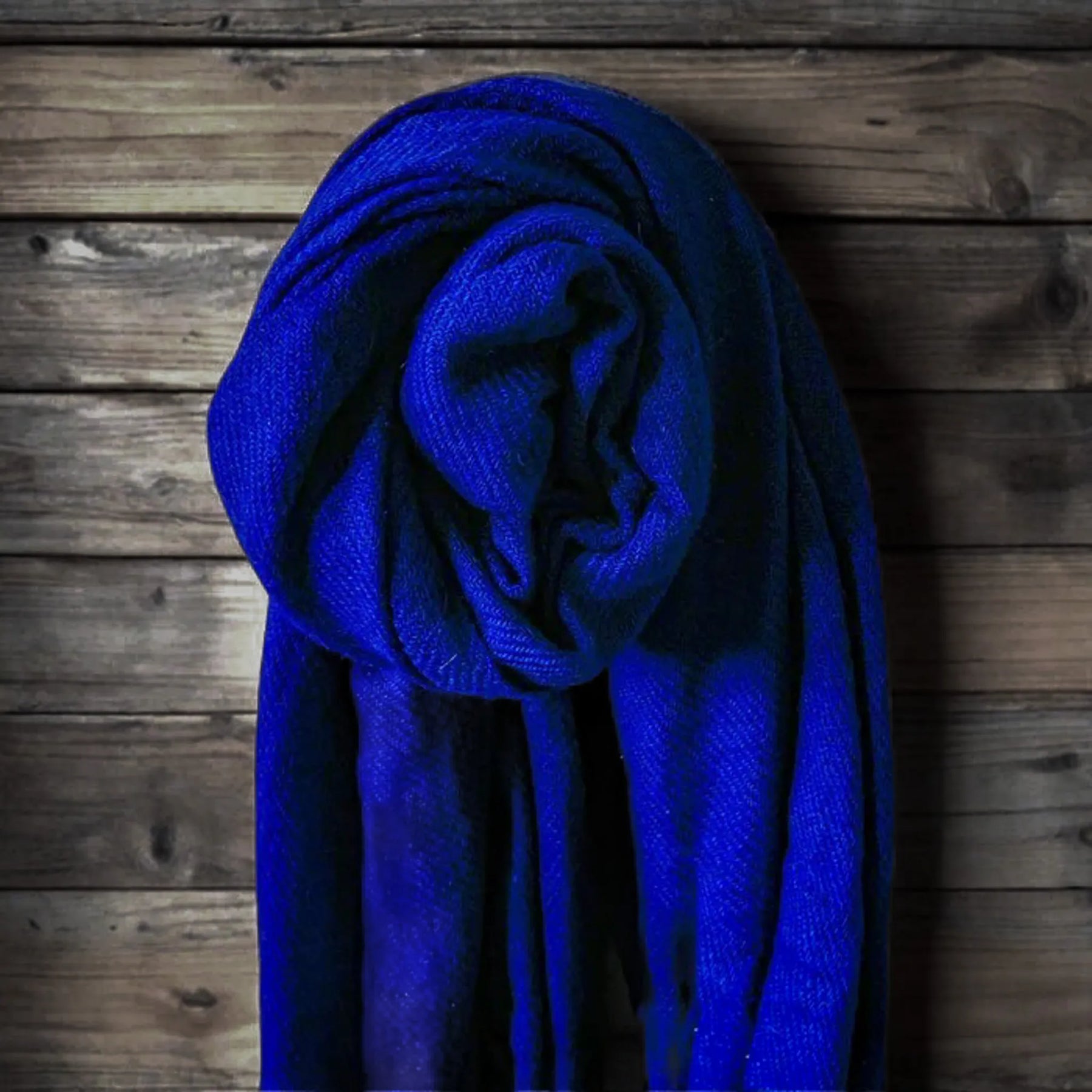 Kornblå kashmirlans präsenterad i upprullad form på träbakgrund visar rik färg och kashmirkvalitet