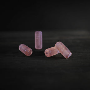 Närbild av fyra cylindriska glaspärlor i ljusrosa färg, perfekta för smyckesbindning. Var pärla är två centimeter långt och sju millimeter bred med två millimeter hål. Det mjuka rosa glaset har en elegant, genomskinlig kvalitet.