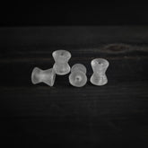 Fyra spolformade pärlor i frostad vitaktig genomskinlig material arrangerade i rad. Varje pärla är cirka 1,7 cm lång och 1,5 cm i diameter med 2 mm genomborrade hål. Studio-produktfotografi mot mörk bakgrund.