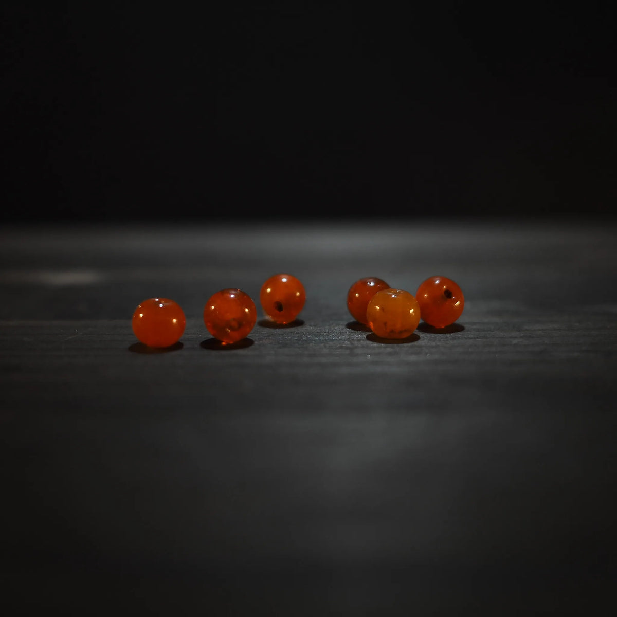 Rund orange pärla - Round orange glass beads (6mm) on dark wood. Warm translucent amber glass beads for jewelry and craft applications.