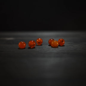 Rund orange pärla - Round orange glass beads (6mm) on dark wood. Warm translucent amber glass beads for jewelry and craft applications.