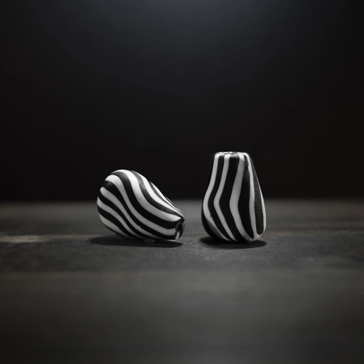 Två zebrarandiga glaspärlor med djärv svartvit randig mönster. Stora pärlor i oval form, cirka 20x28mm, fotograferade på mörk bakgrund för att visa det karakteristiska stripemönstret.