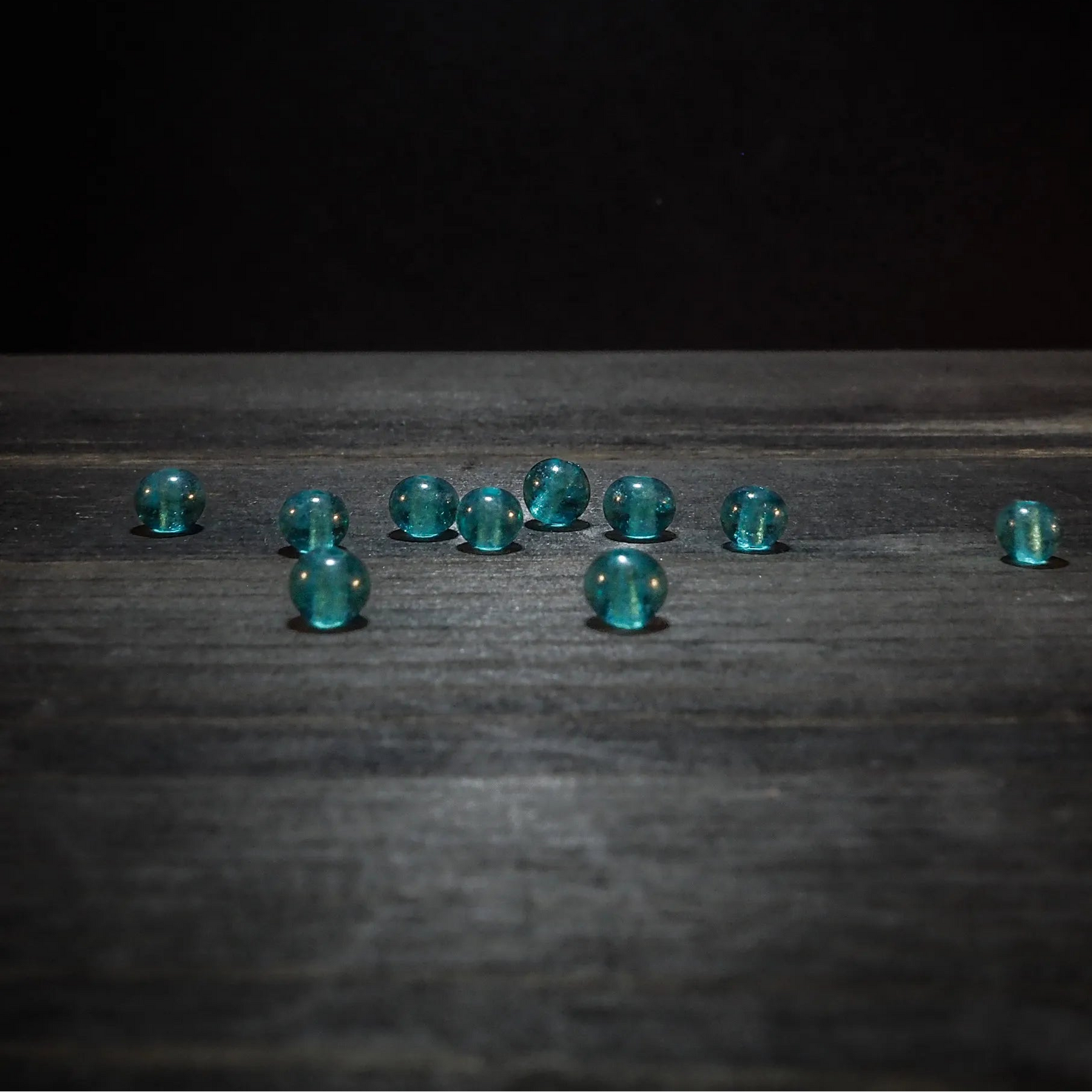 Tio små turkosglaspärlor med hål på träyta