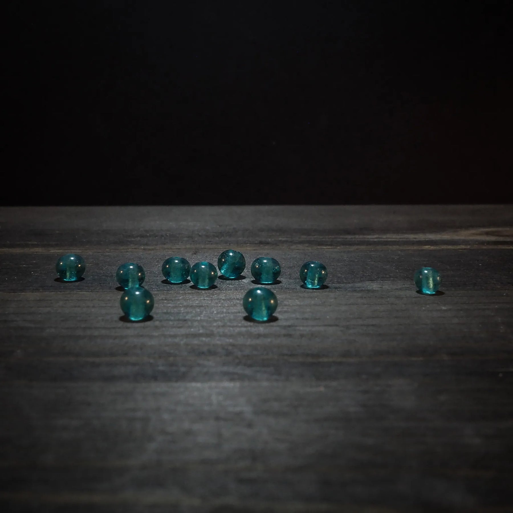 Tio små turkosglaspärlor med facetterad struktur på träyta