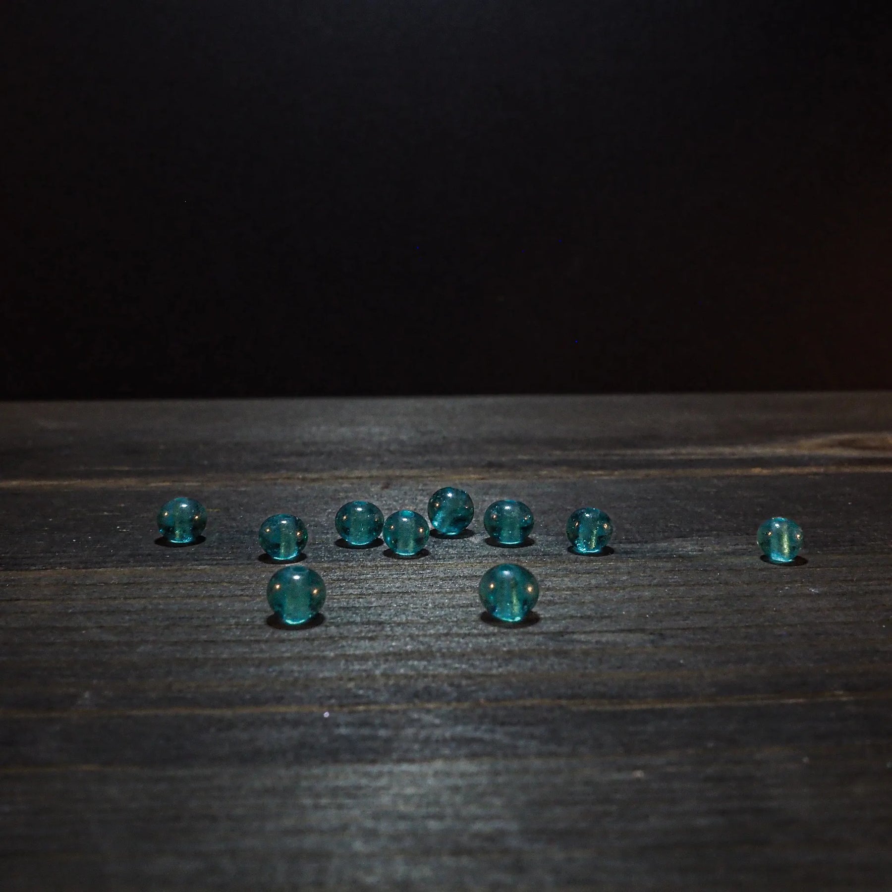 Cirka 10-12 små turkosglaspärlor på träyta