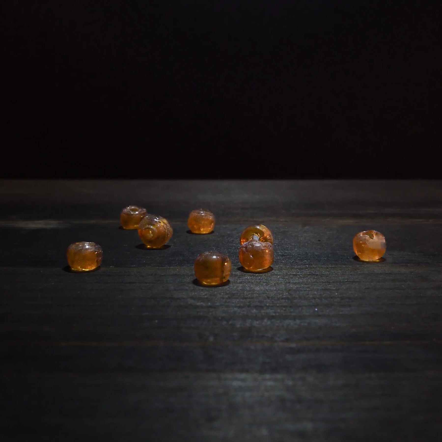 Amber-coloured glass bead – seven beads scattered on a dark wooden surface