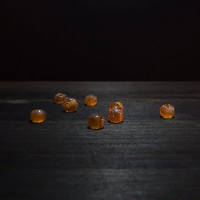 Amber-coloured glass bead – seven beads scattered on a dark wooden surface