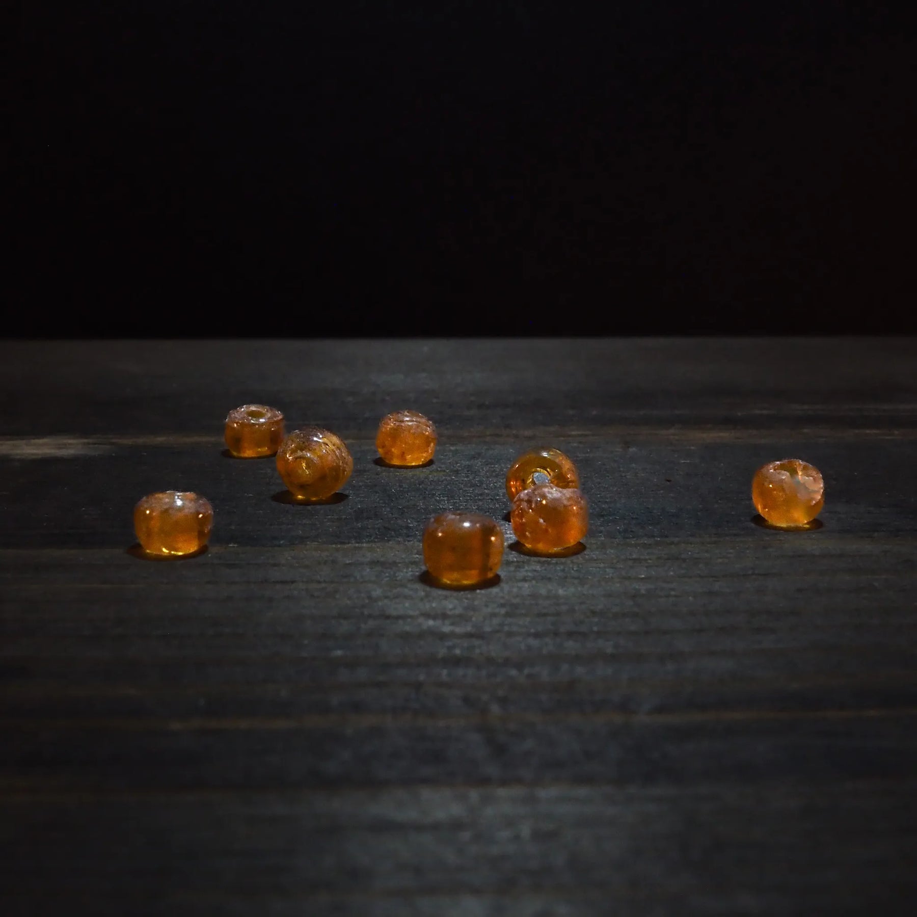 Rund orange glaspärla - Round orange glaspärlor (5mm) arrangerad on dark trä. Translucent amber glass med warm golden tone, perfect for jewelry crafting.